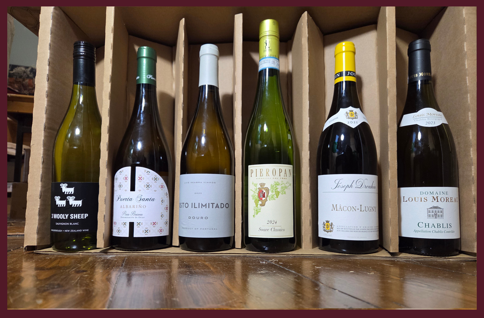 Six wine bottles in a cardboard holder on a wooden surface