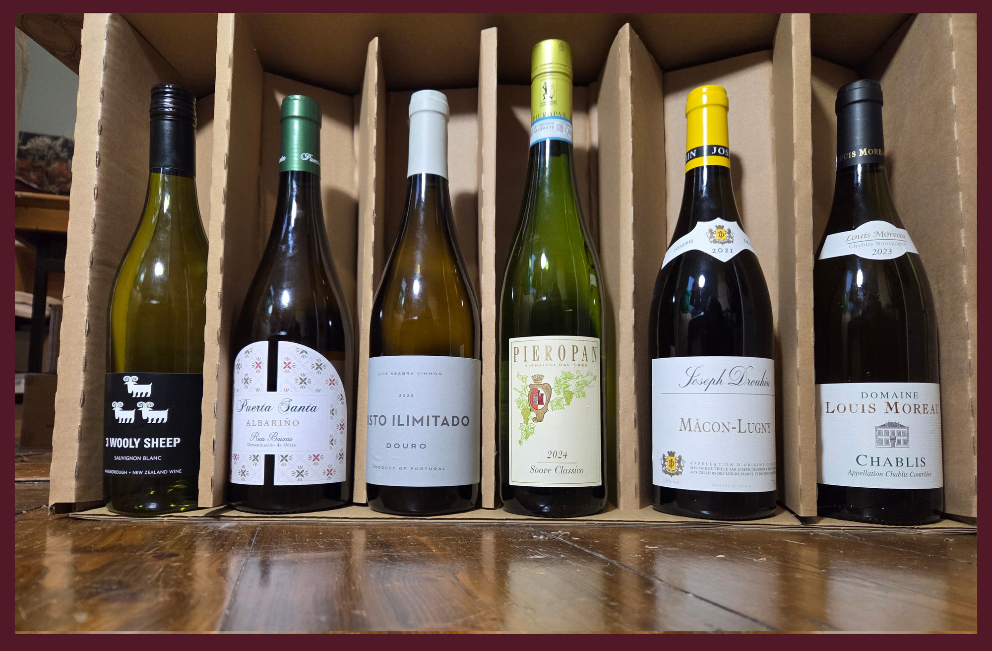 Six wine bottles in a cardboard holder on a wooden surface