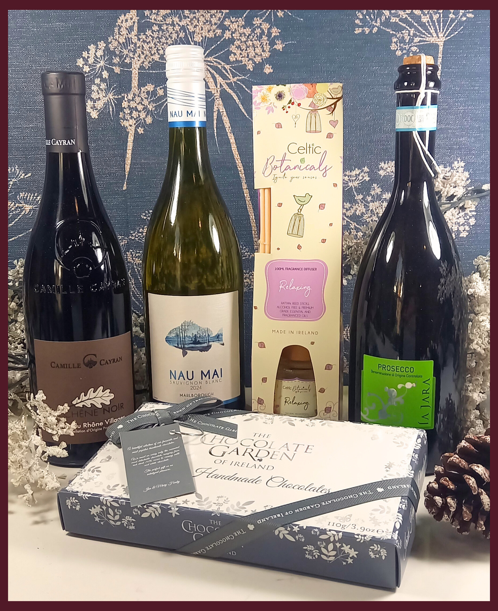 Three wine bottles and a box of chocolate on a decorative background with flowers and pine cones.